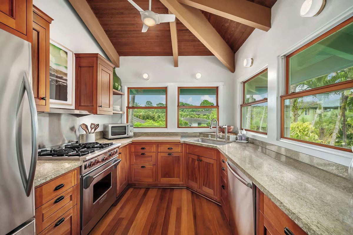 Chef's kitchen with koa cabinetry, gas range, stone counters and a window over the sink looking into the valley.