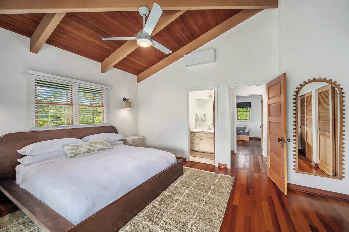 Primary bedroom with a king bed, wood floors, a wool rug and an arched mirror by the doorway.