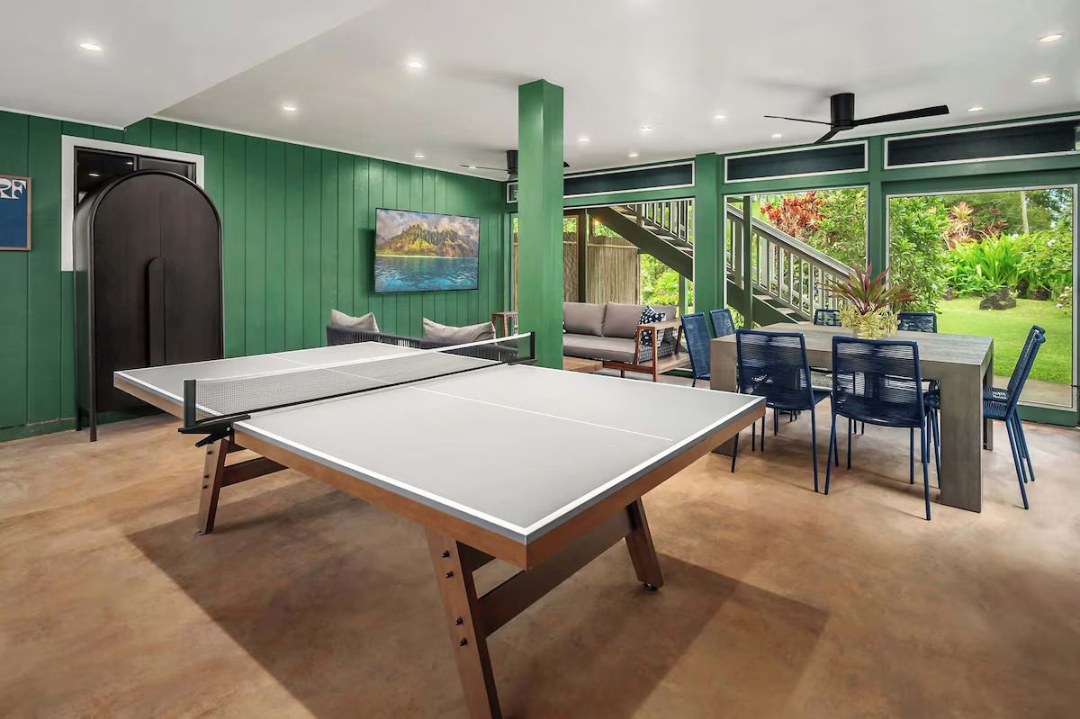 Downstairs recreation room painted deep green, with a ping-pong table, smart TV, sofa and a long dining table.