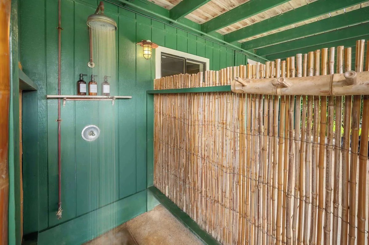 Private outdoor shower with a copper rain head, green board-and-batten walls and a bamboo privacy screen.