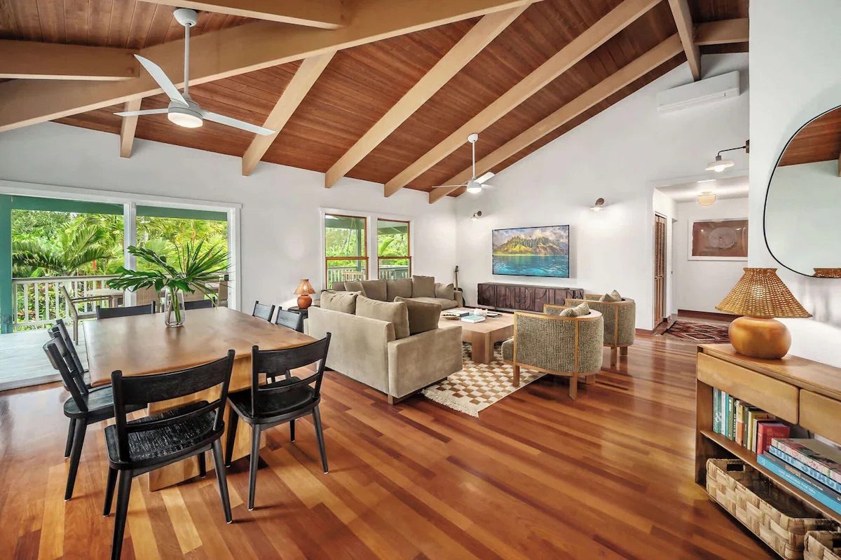 Living room with deep sofas, rattan armchairs, a carved wood console and a checkered wool rug.