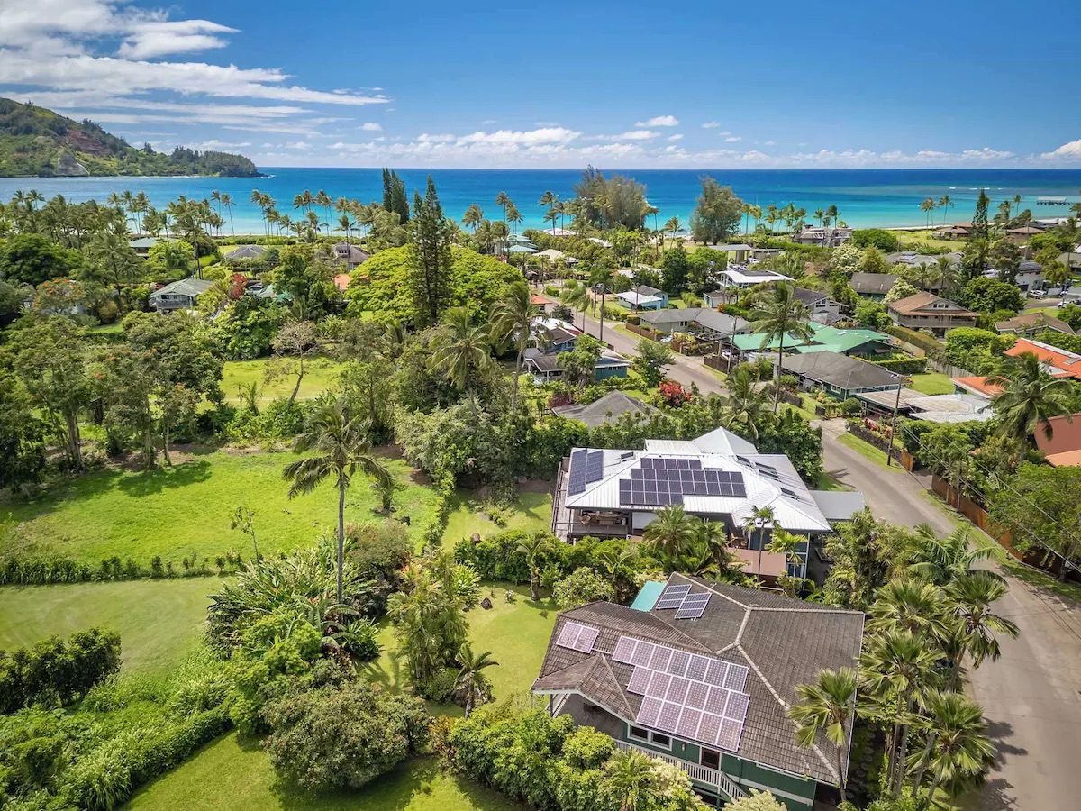 Aerial view of the house on Aku Road with Hanalei Bay's turquoise water and the pier just beyond the treeline.