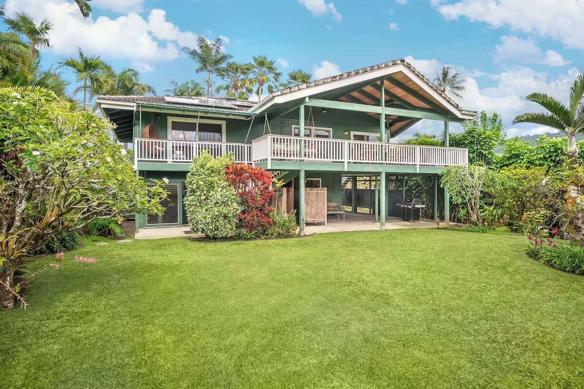 The green plantation house seen from the lawn, with its double-height lanai and palms on either side.