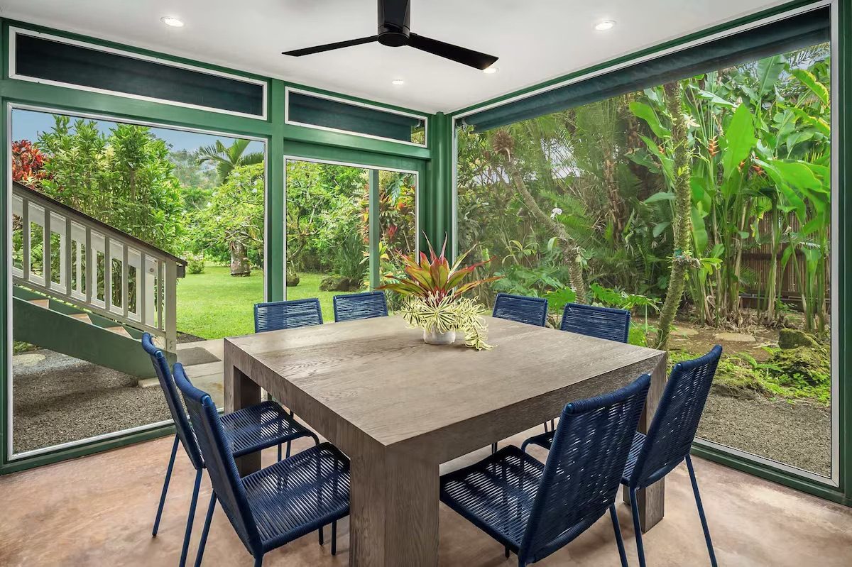 Concrete dining table with blue rope chairs on the screened lower lanai, opening to the lawn.